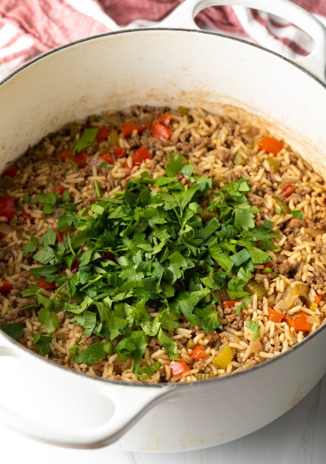 Cooked dirty rice in a pot topped with fresh parsley. 