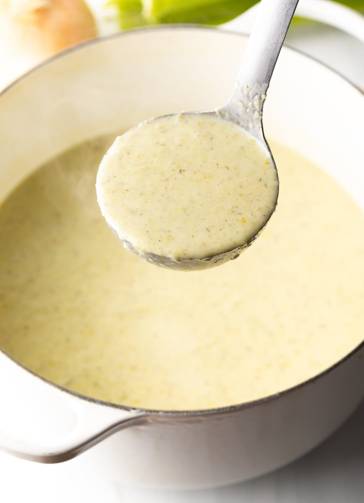 Metal ladle with cream of celery soup held to camera.
