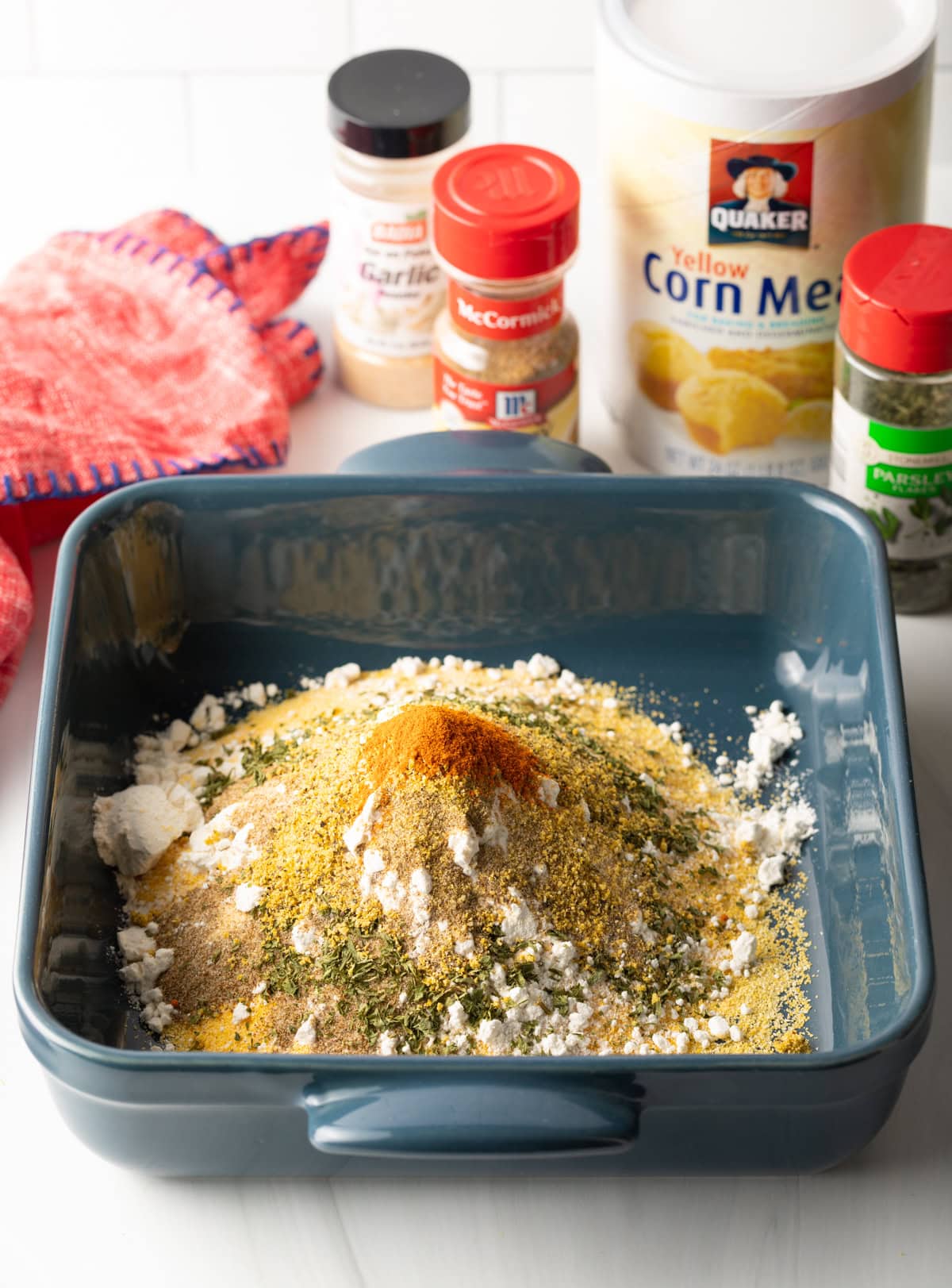 Cornmeal, flour, spices and fresh herbs in a blue square baking dish.