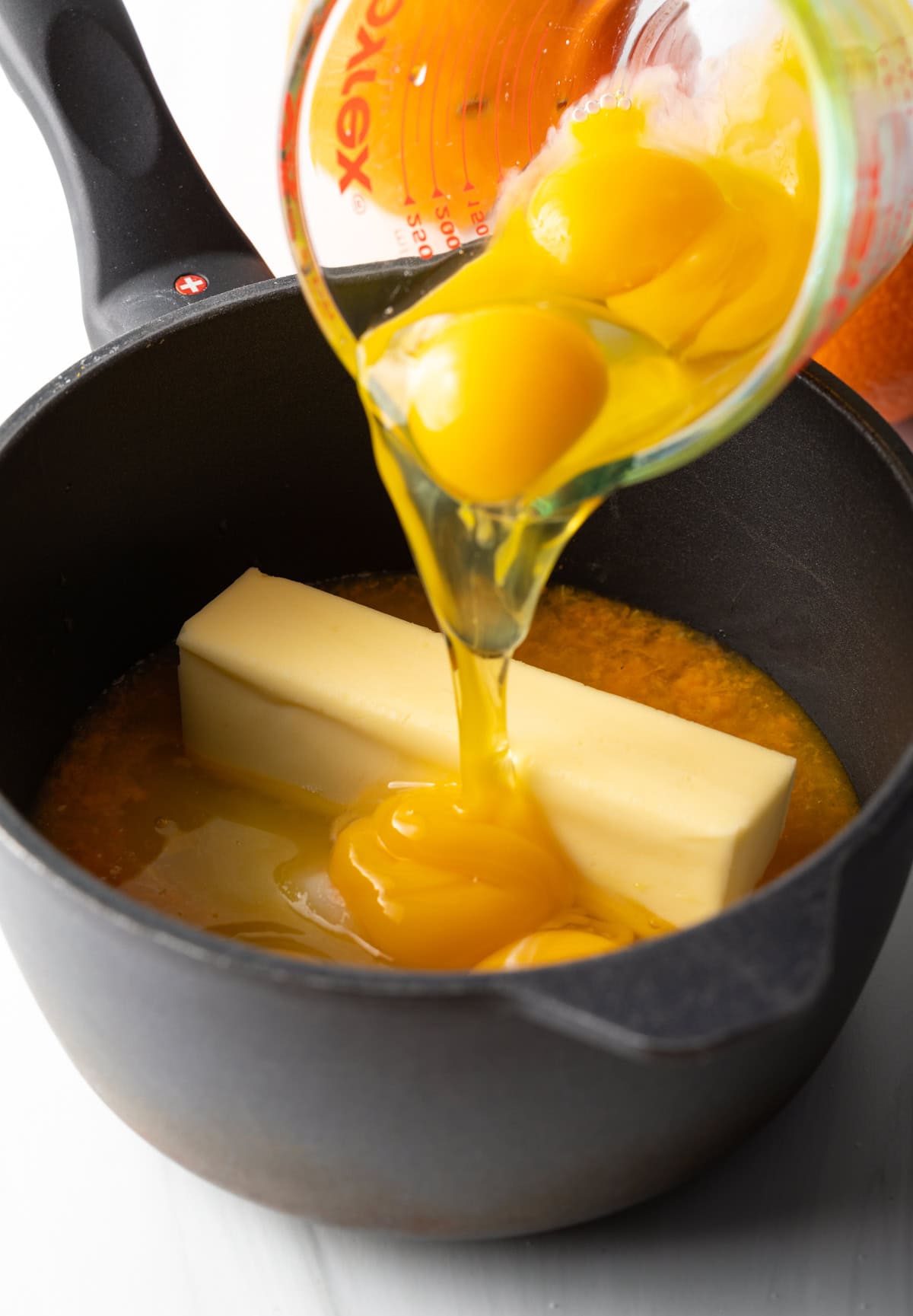 Eggs being poured into a saucepan that already has juice, butter and zest in it.