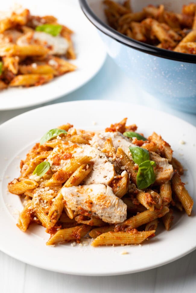 Plated pesto pasta with chicken on a white plate.