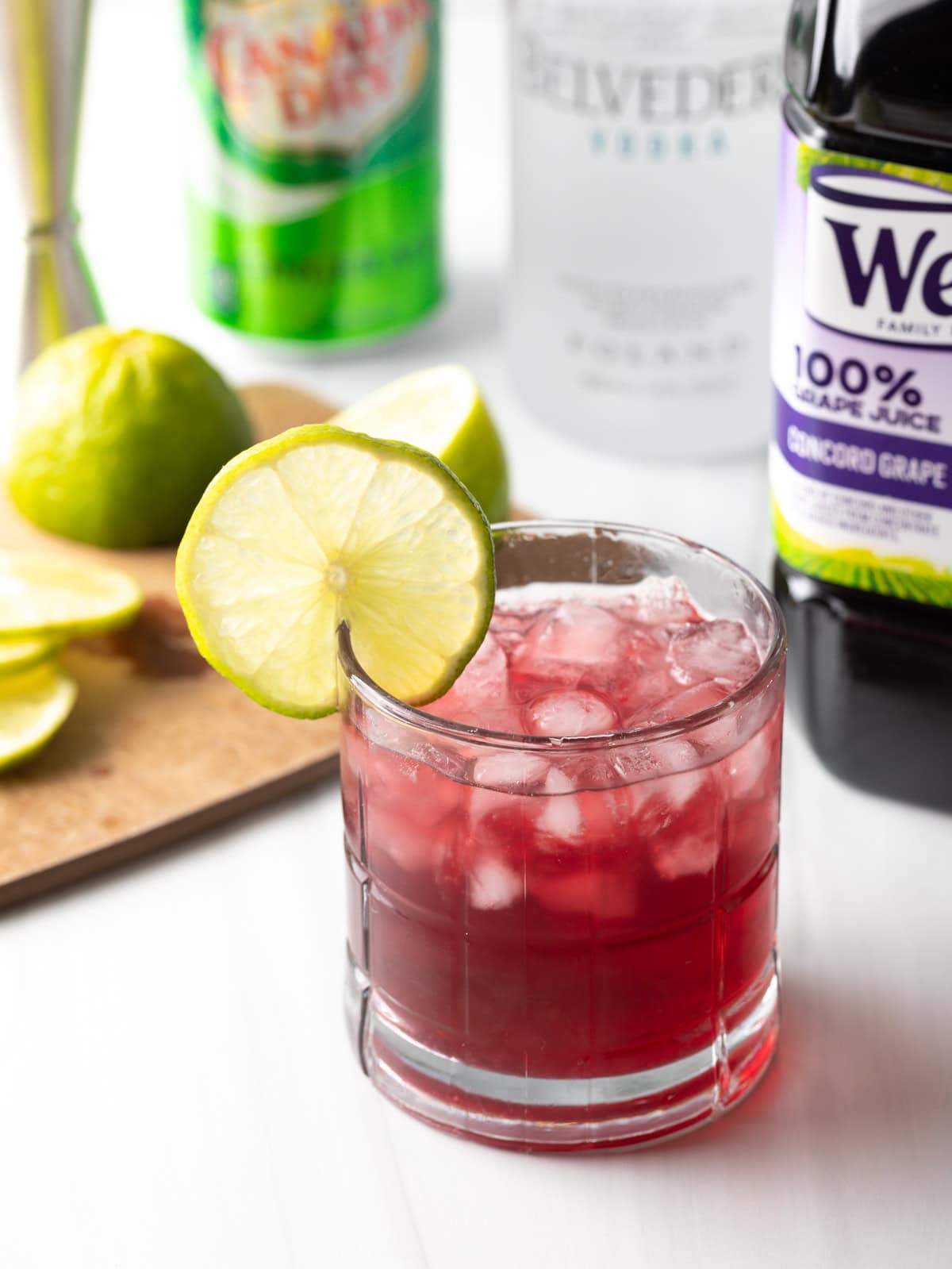 Full shot of transfusion drink garnished with lime, ingredients in background.