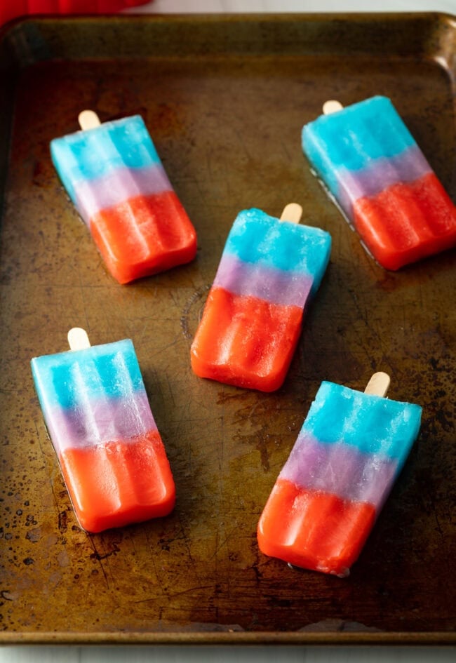 Rainbow popsicles on a rimmed baking sheet.