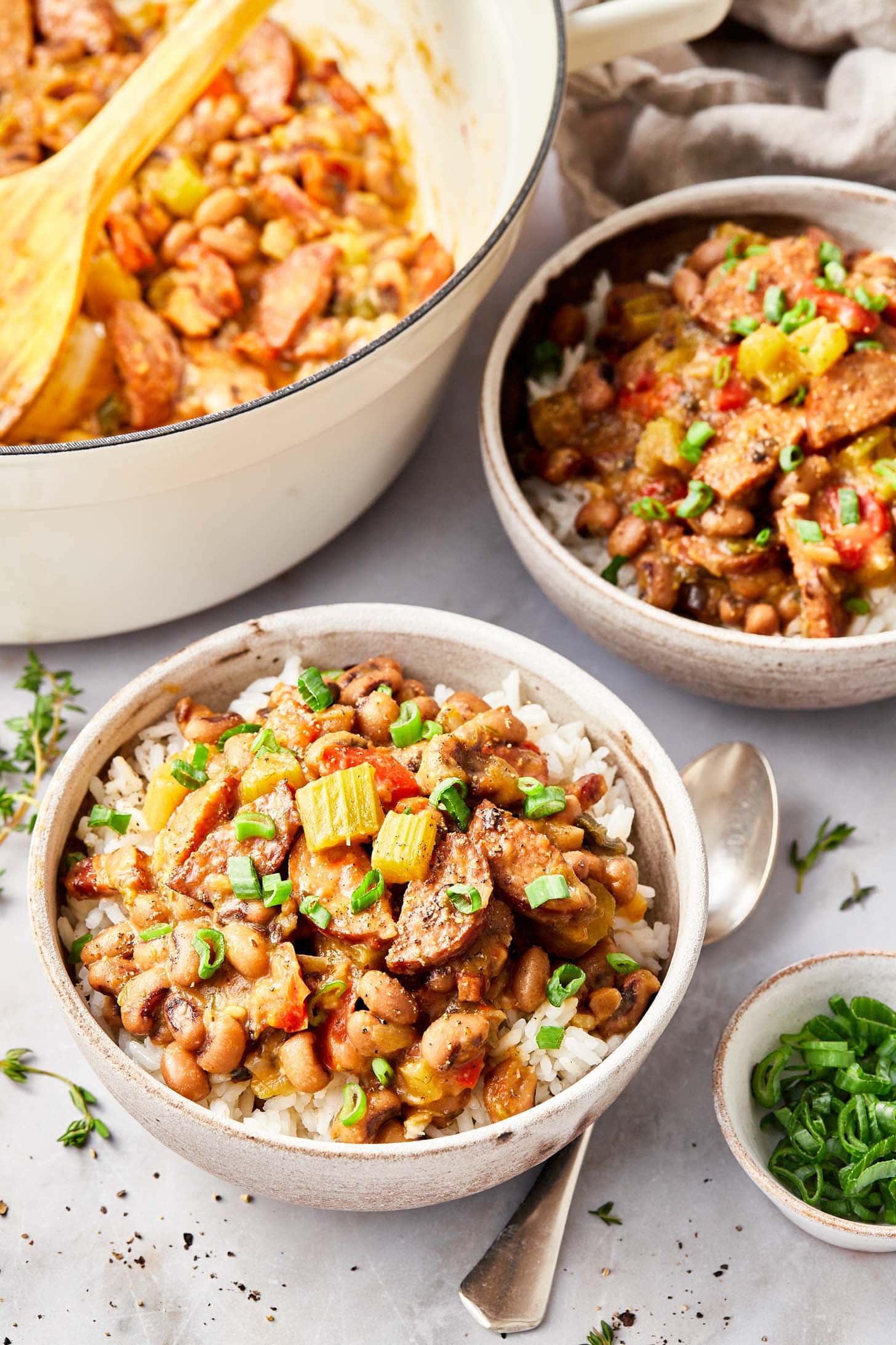 Closeup of hoppin john over rice served in a bowl with a small ramekin filled with fresh sliced green onion next to it.
