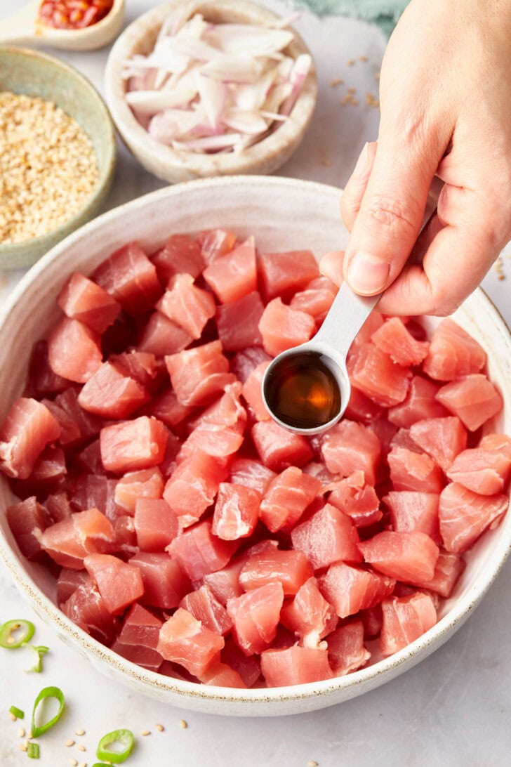Hand pouring sauce over chopped tuna.