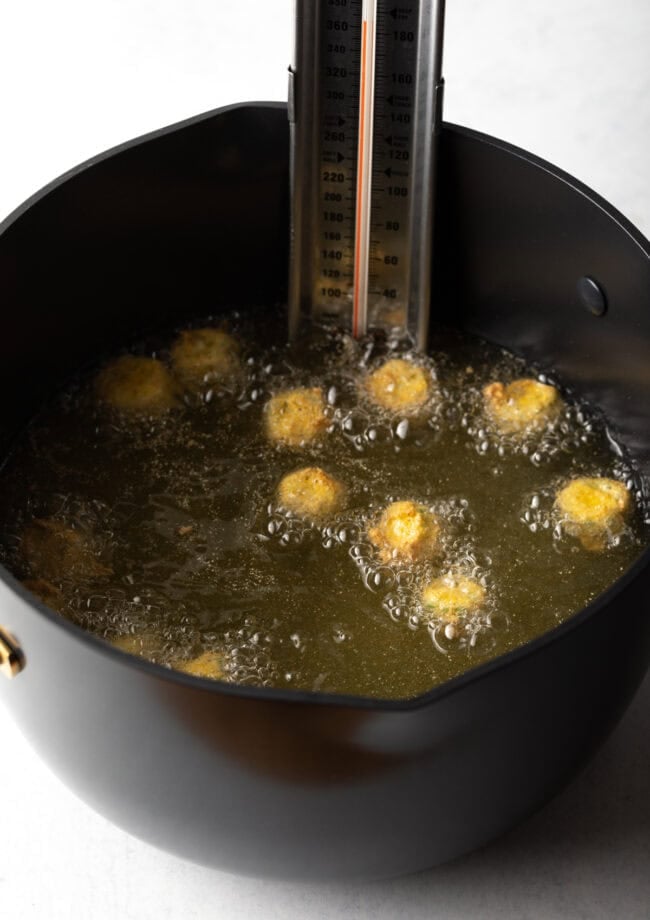Hot oil in large pot, pieces of breaded okra frying.