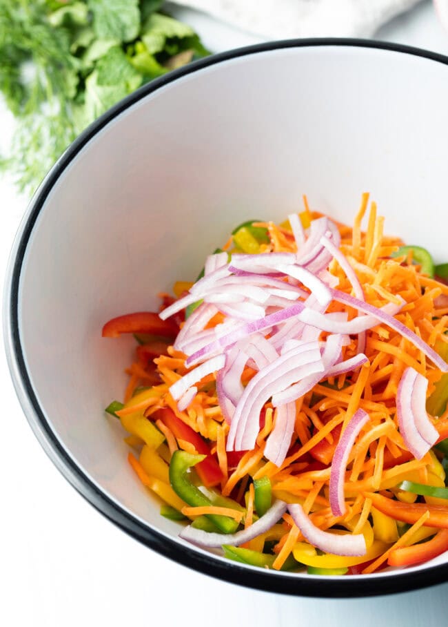 Sliced peppers, carrots and onion in a bowl. 