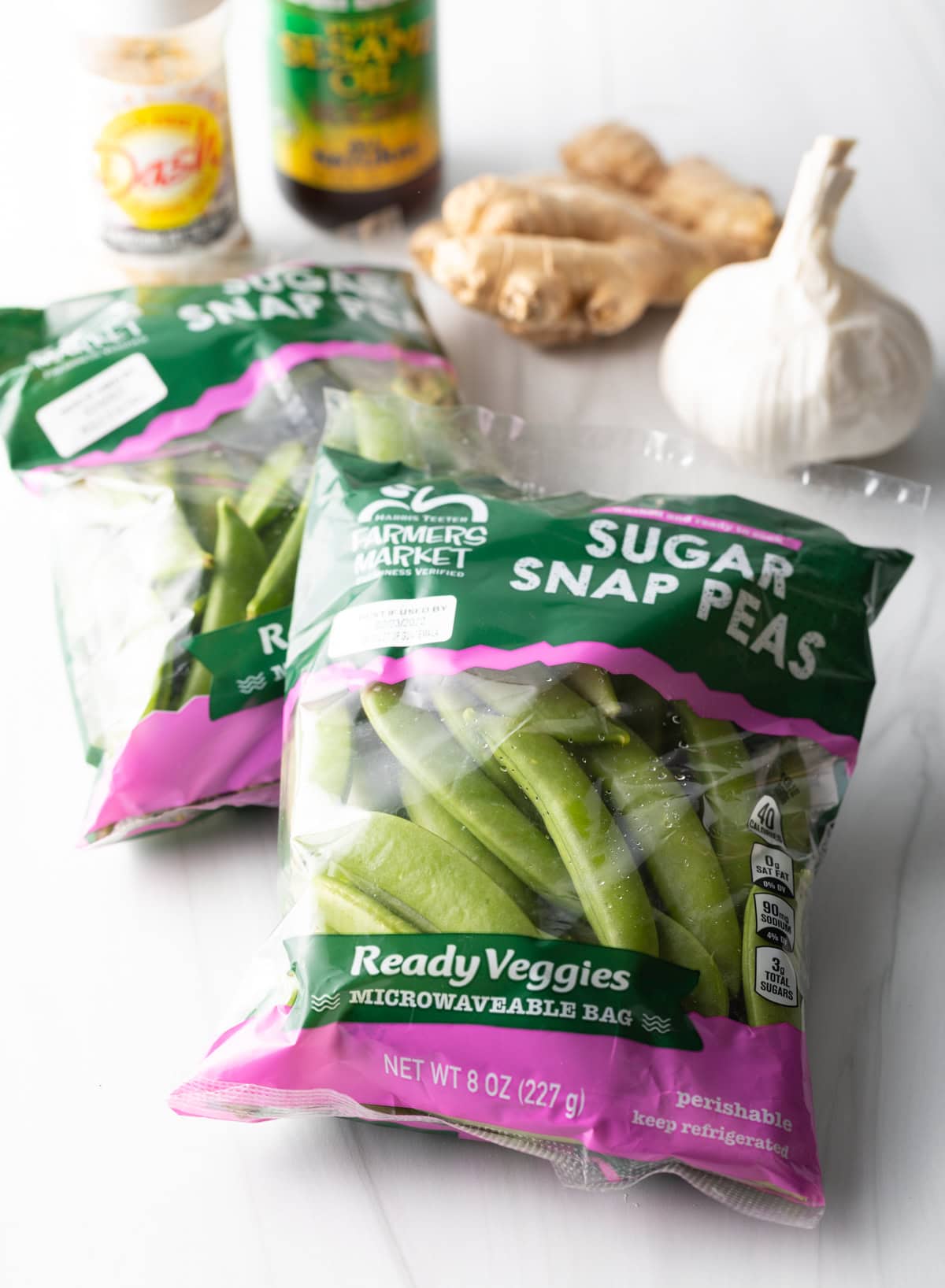 Bag of sugar snap peas, head of garlic, ginger, and seasonings in the background.