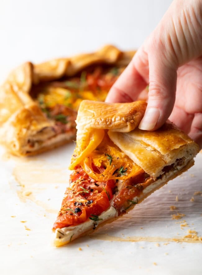 Hand holding slice of tomato galette.