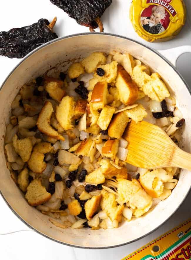 Overhead view of a pot with toasting bread chunks, spices, and fruits in a pot. 