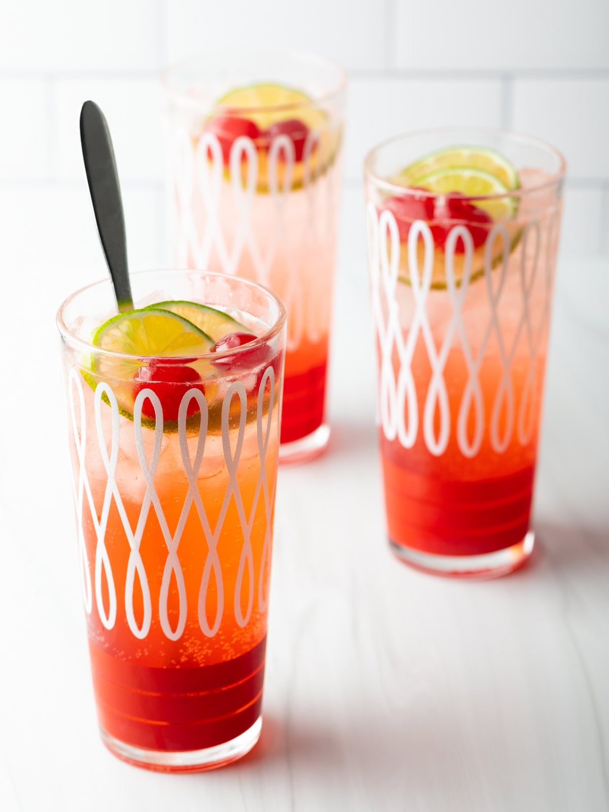 Three glass cups filled with a refreshing cherry limeade recipe, topped with lime wedges and maraschino cherries.