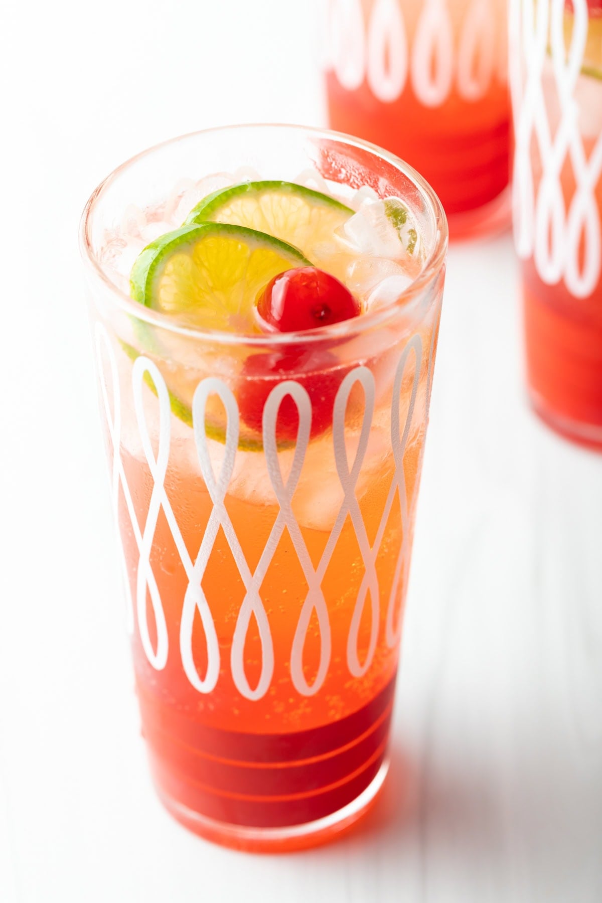 A glass filled with cherry limeade topped with maraschino cherries and lime wedges.