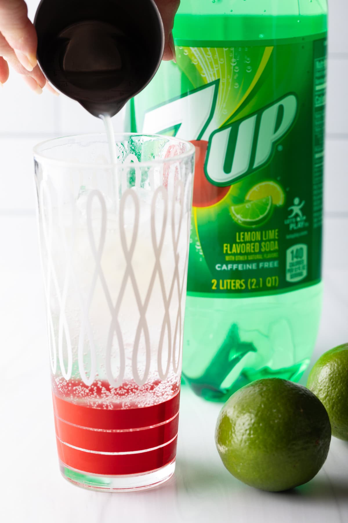 A glass filled with ice with fresh lime juice being poured over the ice.