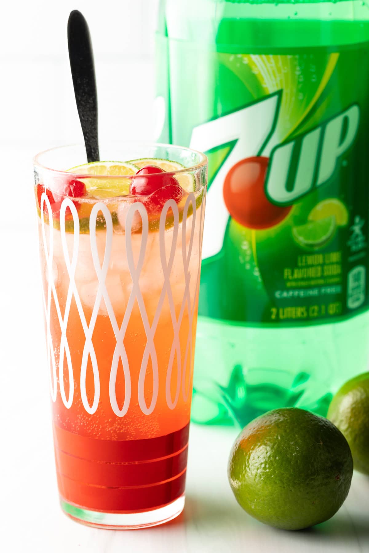 A glass filled with a homemade cherry limeade recipe, with a long spoon for stirring.
