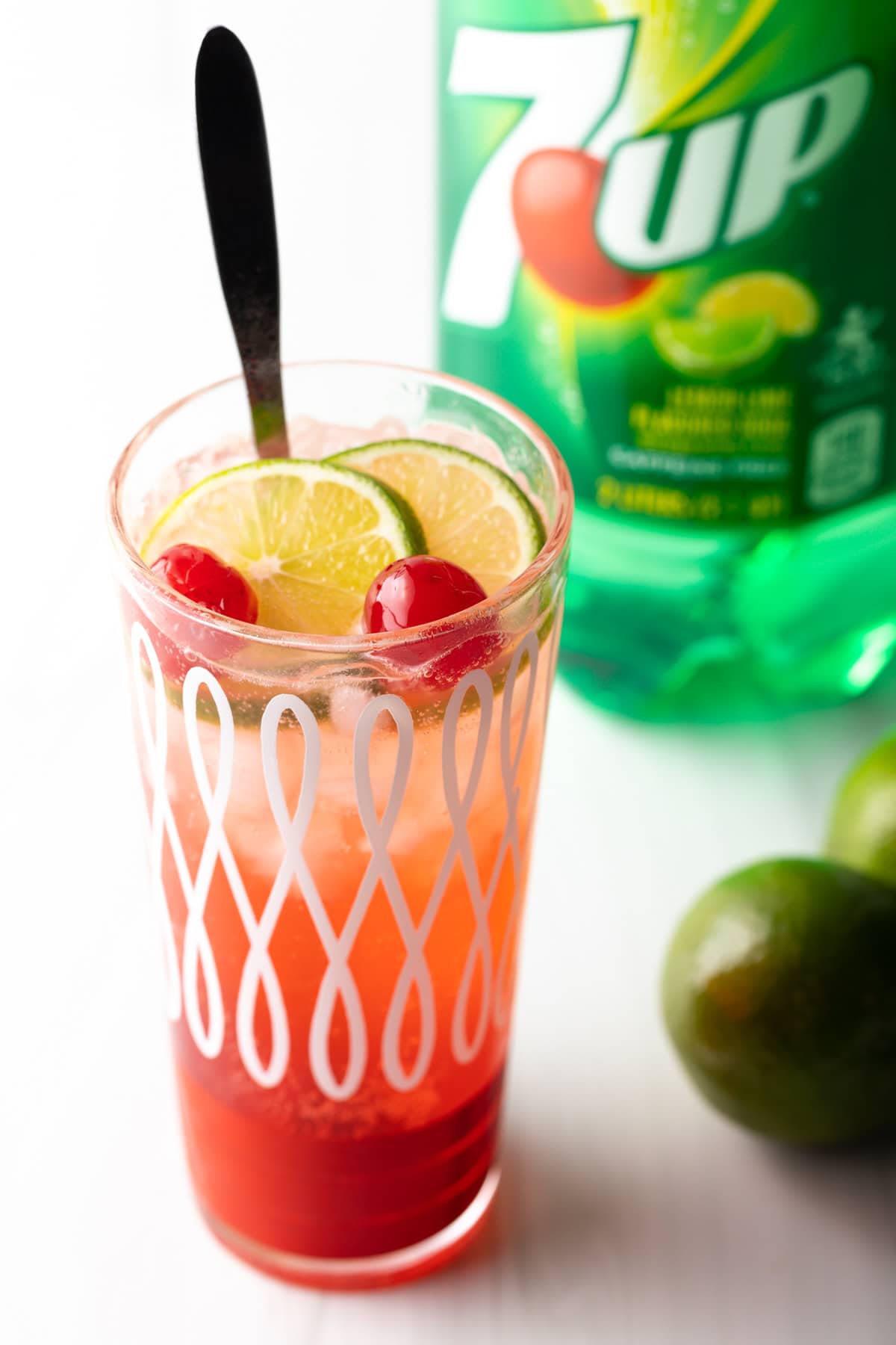 A glass filled with an easy cherry limeade recipe, with a long spoon for stirring.