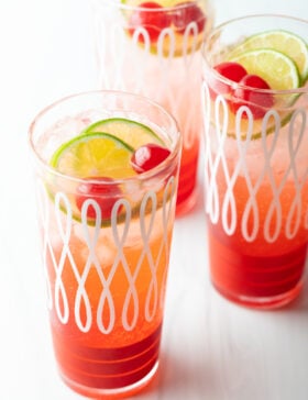 Three glass cups filled with a refreshing cherry limeade recipe, topped with lime wedges and maraschino cherries.