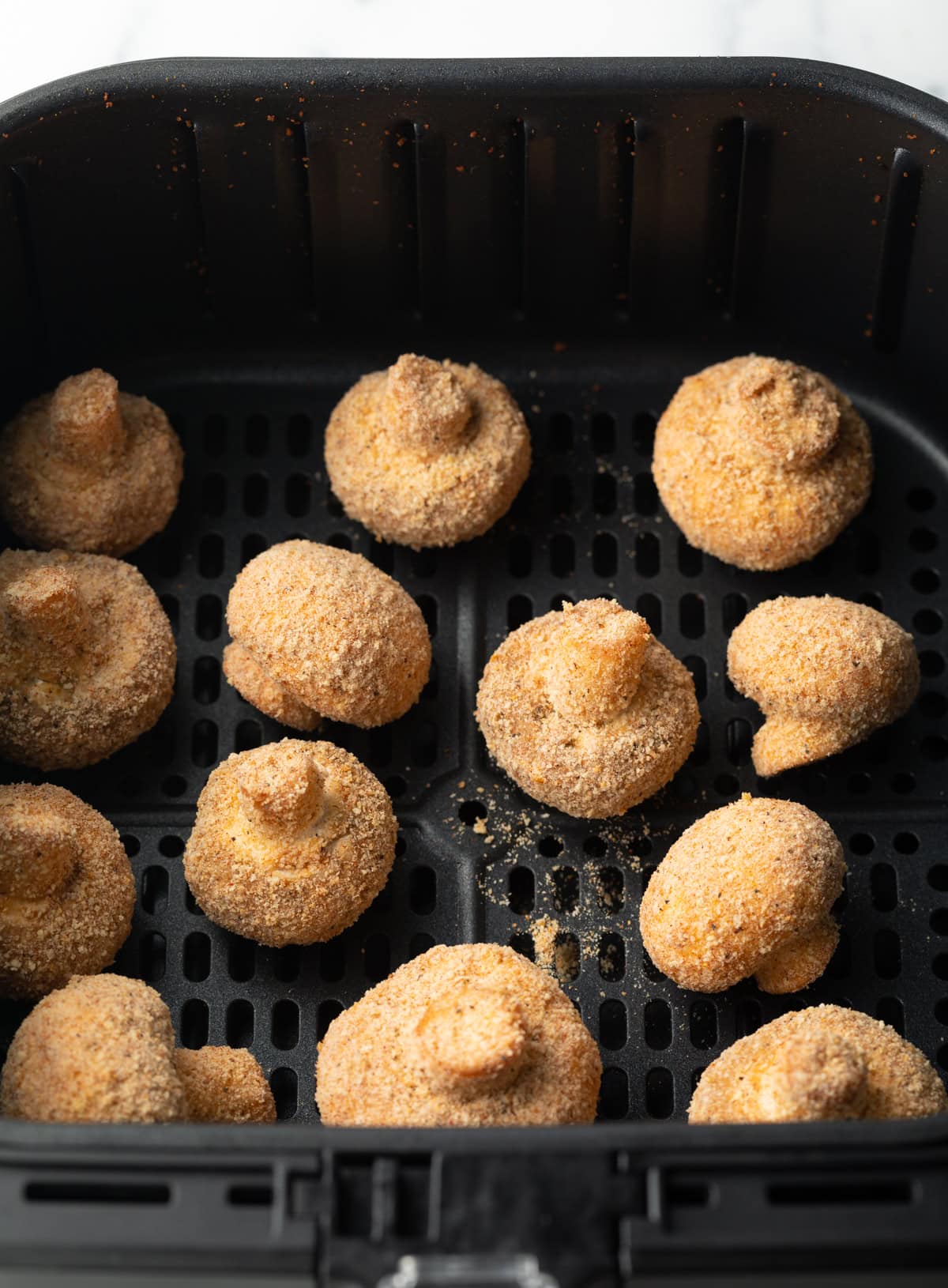 Battered mushrooms in the air fryer basket.