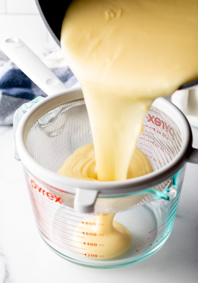 Pudding mixture being poured through a strainer and into a glass container.