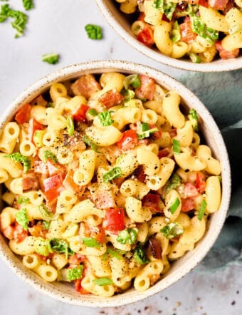 Overhead image of a macaroni salad in a white bowl with chopped tomatoes, green onions and kale in a creamy dressing.