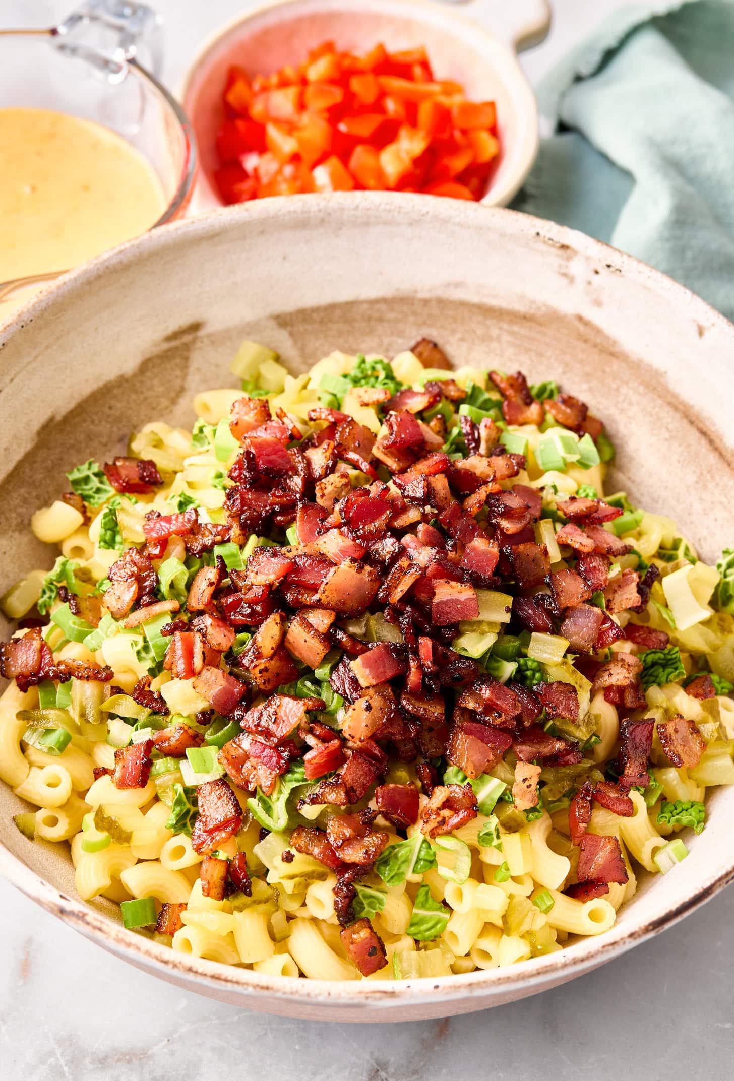 Chopped bacon and kale on top of cooked macaroni elbows in a serving bowl.