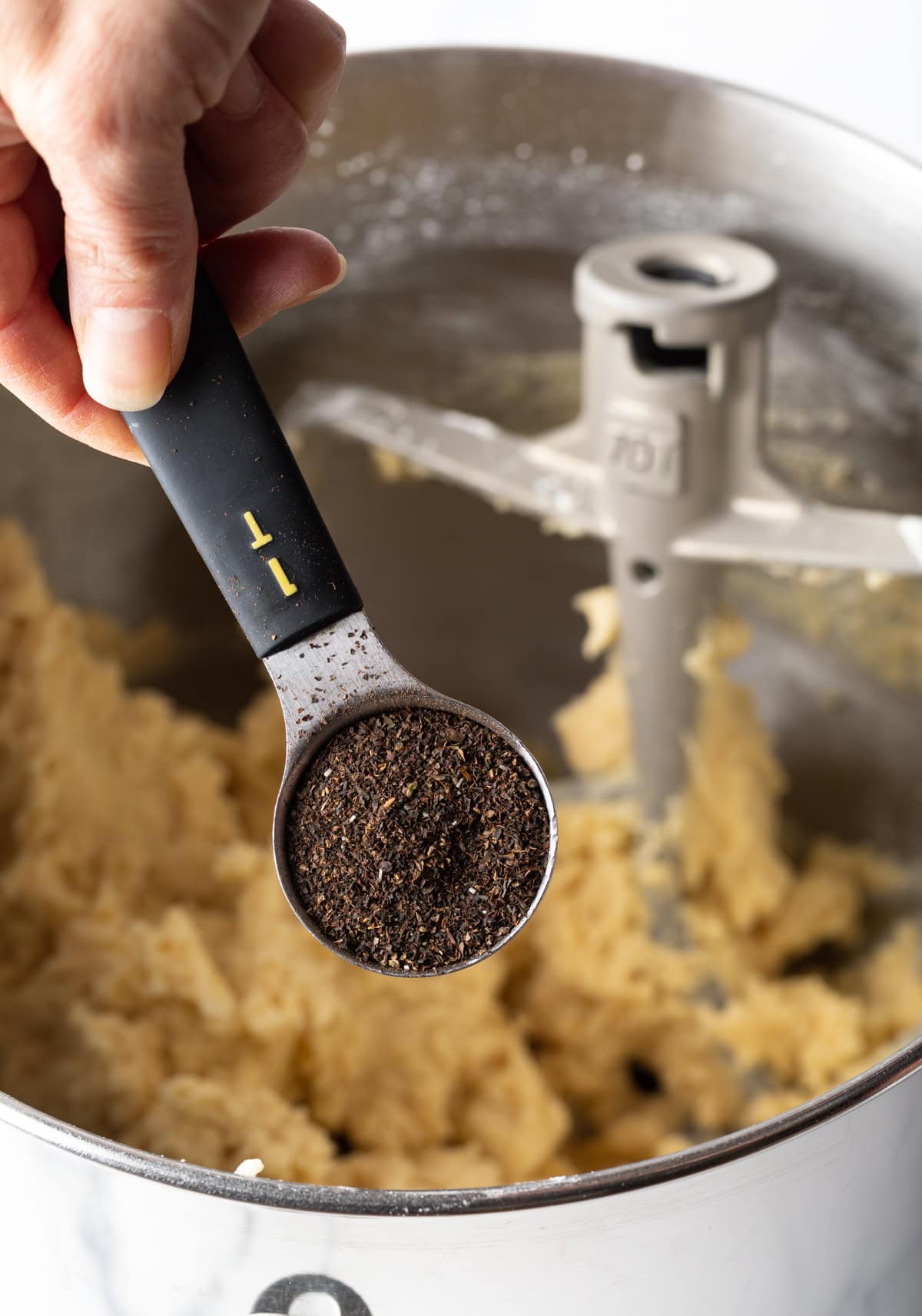 Teaspoon with earl grey tea leaves above a bowl of cookie dough.