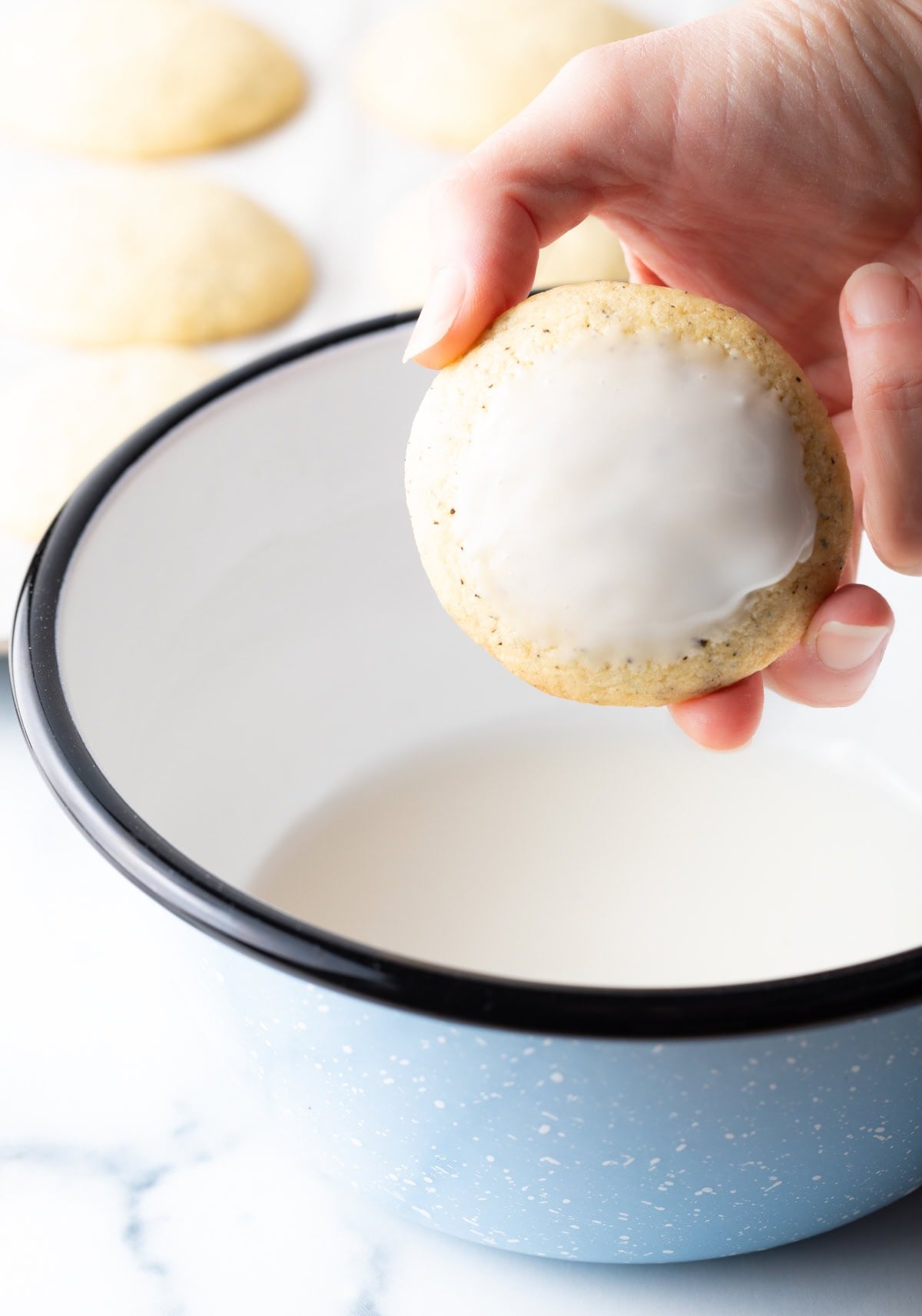 Hand holding a dipped cookie to camera over a bowl of glaze.