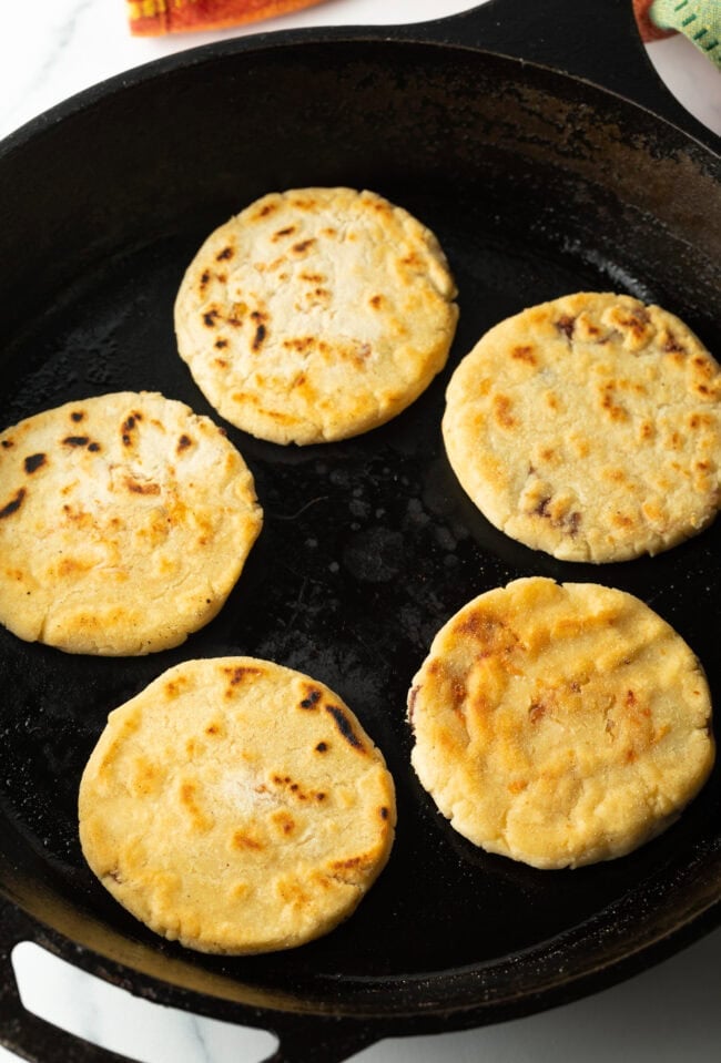 Pupusas cooking in a cast iron skillet.