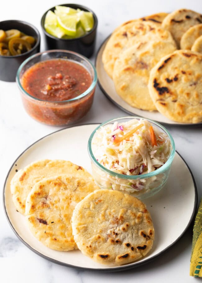 Three pupusas on a plate with small glass dish of slaw.