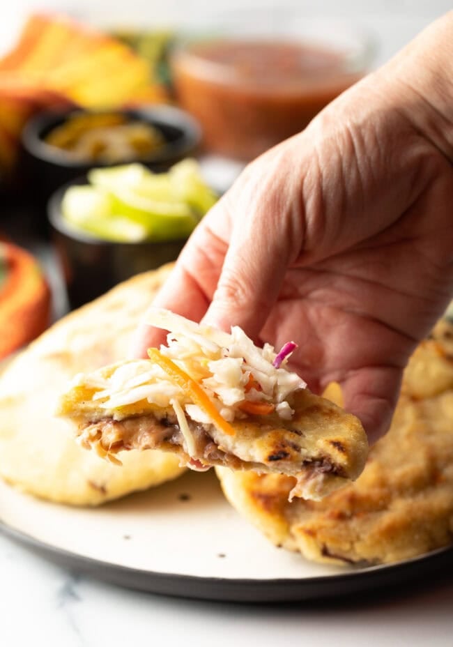Hand with pupusa bite taken, coleslaw on top.