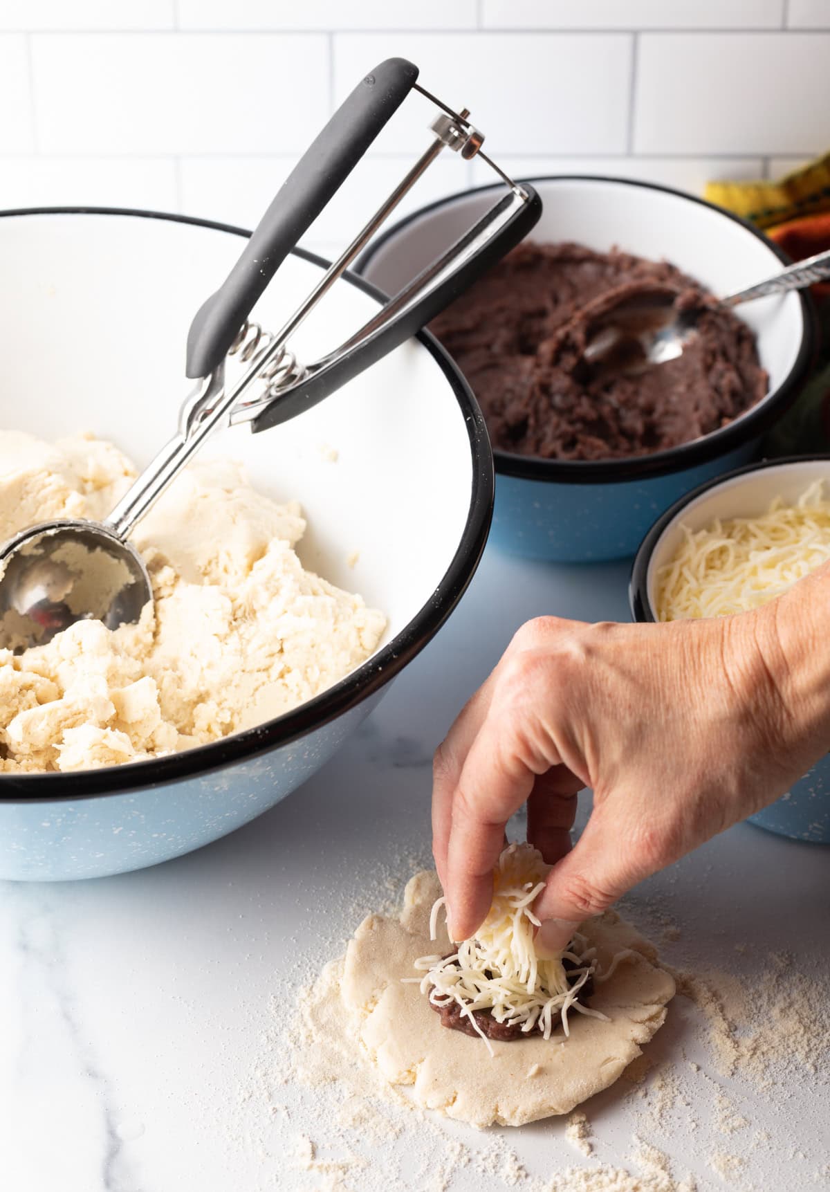 Hand adding shredded cheese to beans on flat dough.