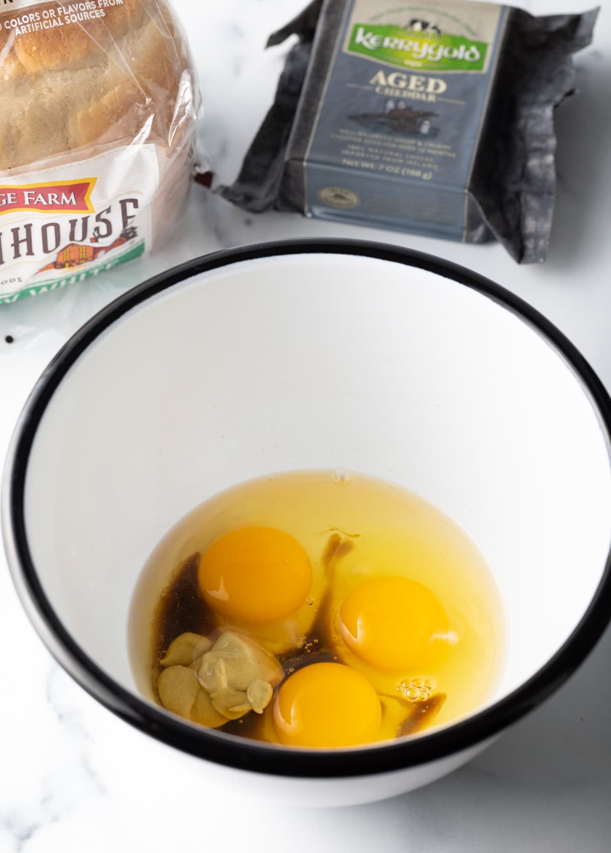Large white bowl with 3 cracked eggs, dijon mustard, Worcestershire sauce.