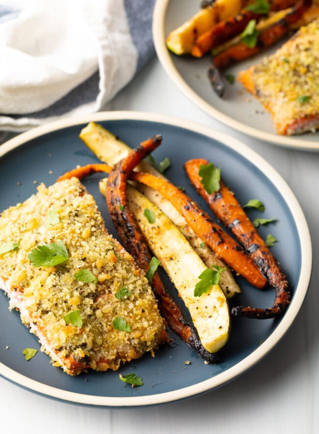 Top down view of baked pesto salmon with panko, grilled veggies on the side.