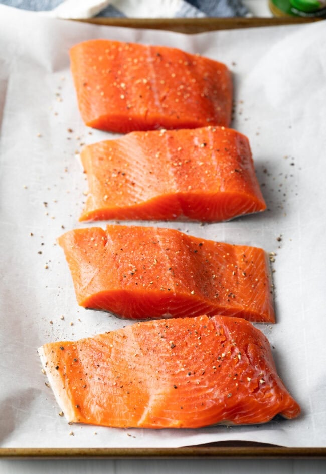 4 fillets of raw salmon on a baking sheet, seasoned with salt and pepper.