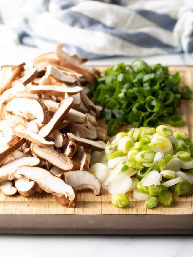 Wooden cutting board with sliced mushrooms and green onions.