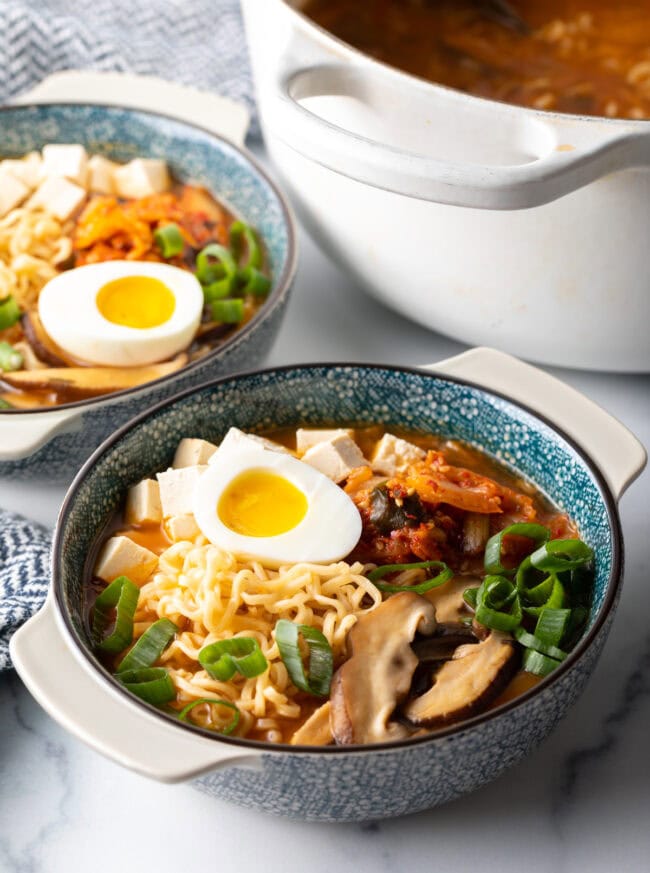 Two bowls of Korean spicy ramen noodle soup with halve of soft boiled eggs on each bowl.