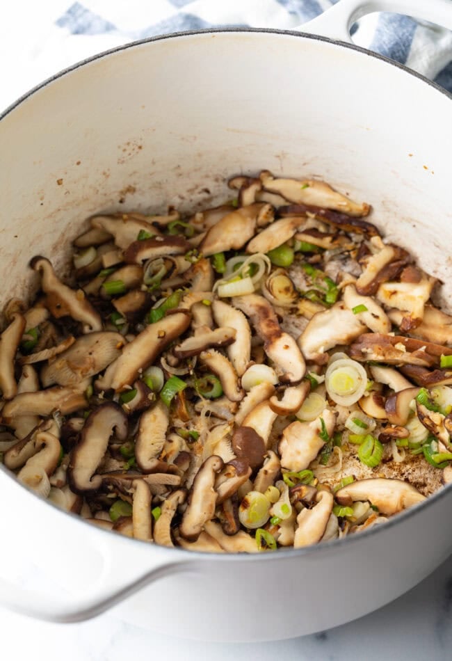 Cooking pot with sliced mushrooms and green onions.