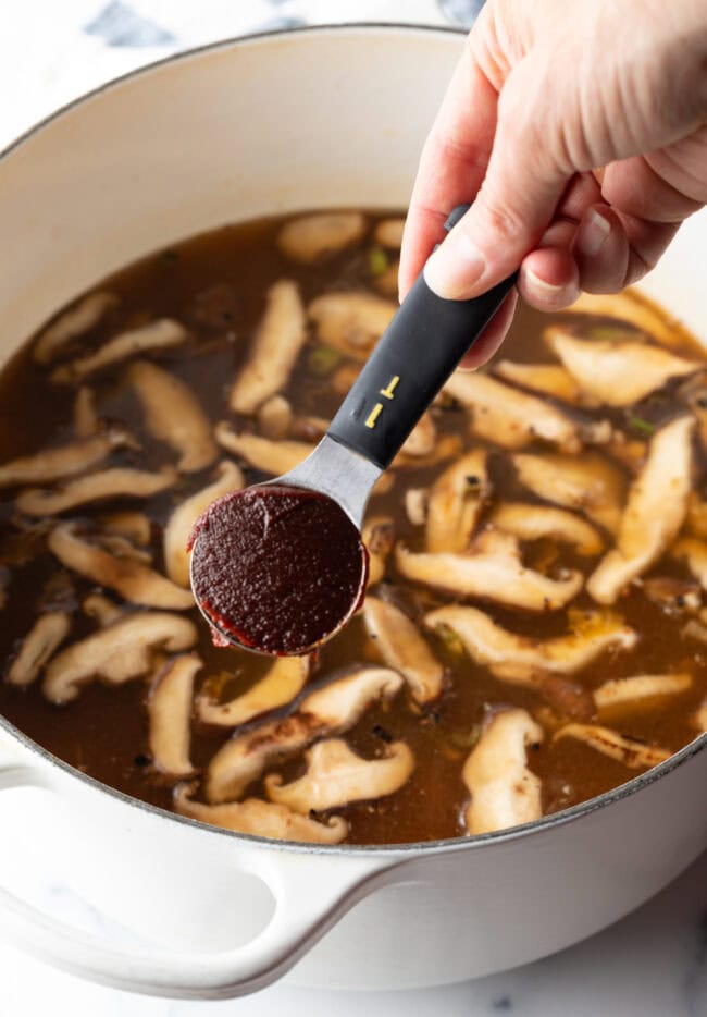 Hand adding 1 tablespoon of gochujang sauce to the cooking pot.