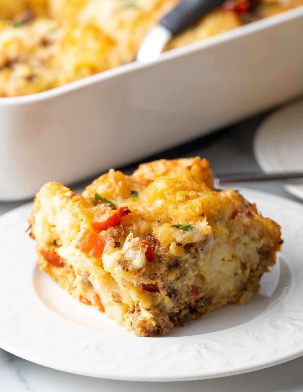 Close view of square of casserole with eggs and tater tots on a white plate.