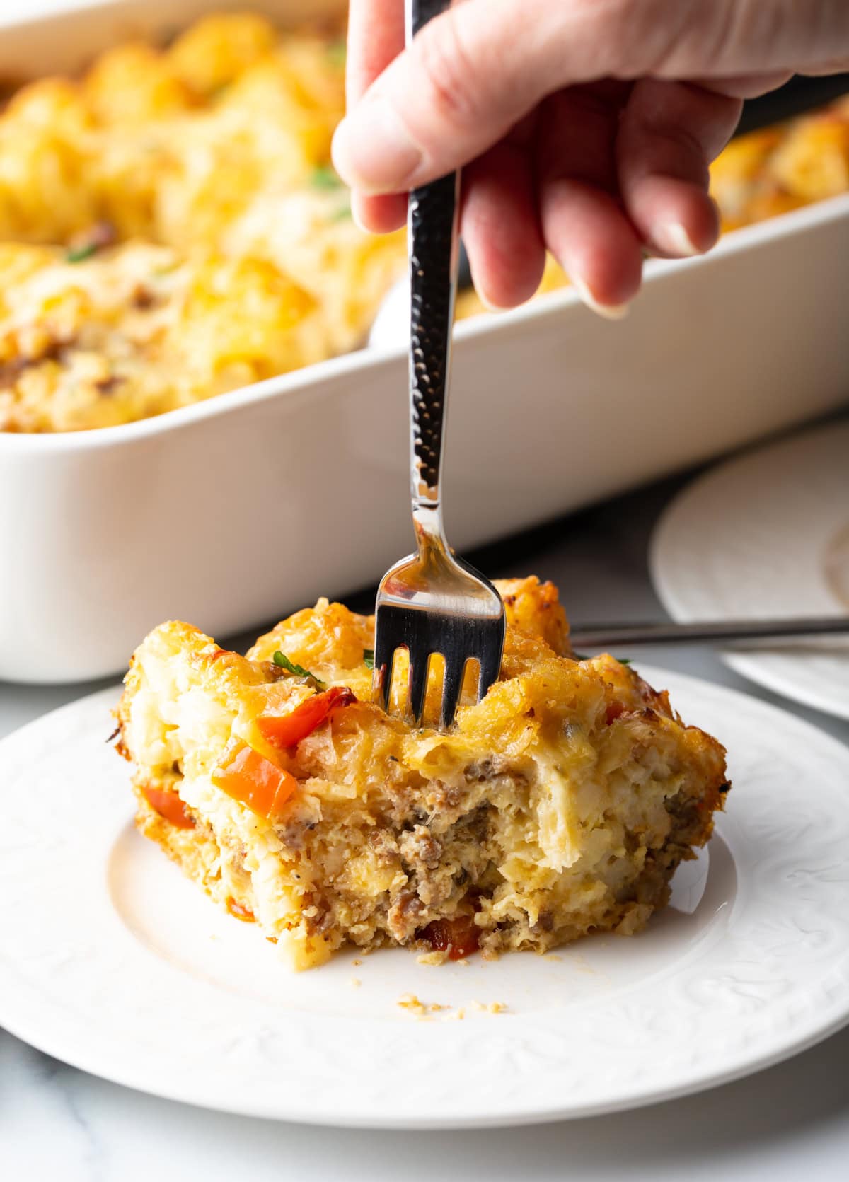 Hand with fork taking bite of wedge of breakfast casserole.