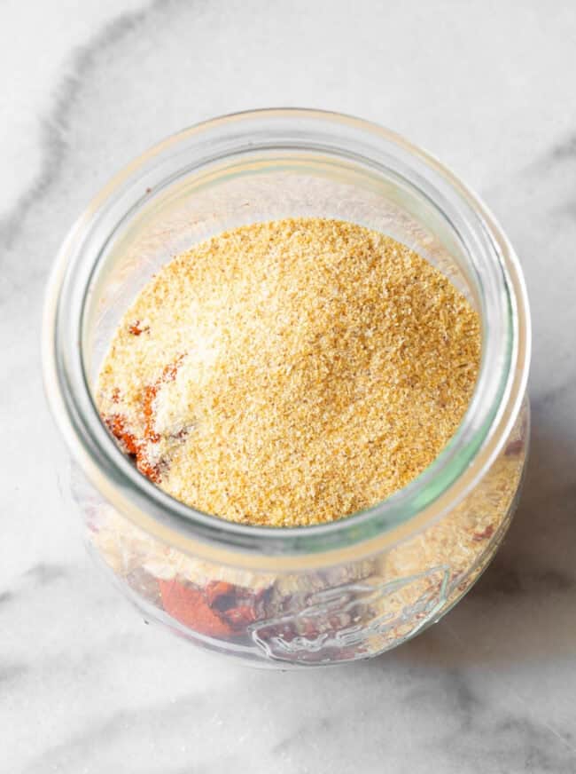 An overhead view of a glass jar full of blackened seasoning. 