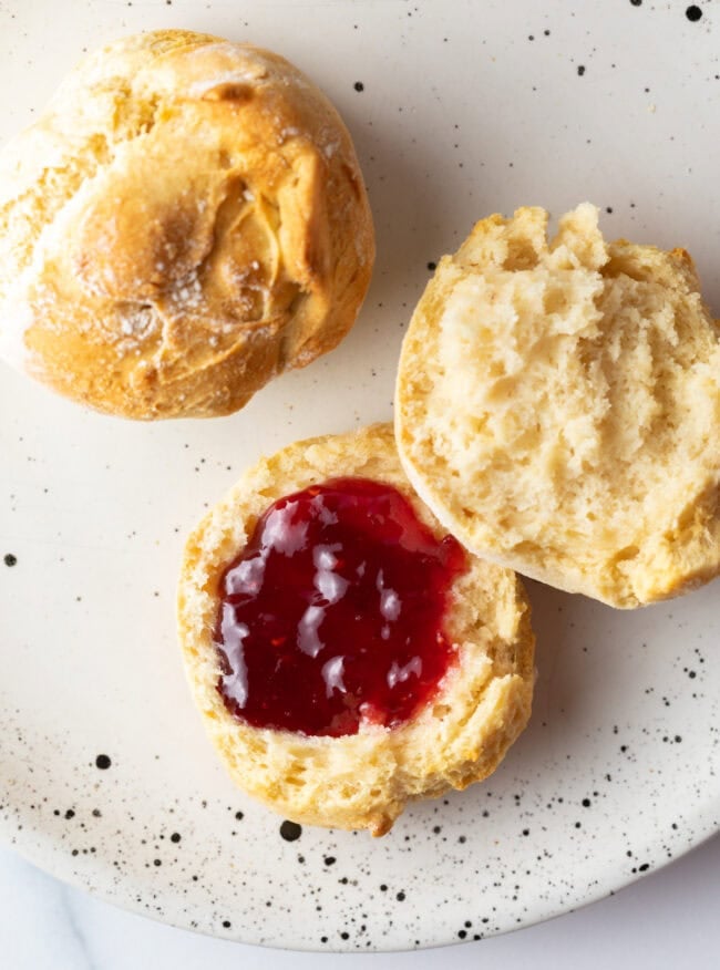 Top down two biscuits on a plate, one split in half with jelly.