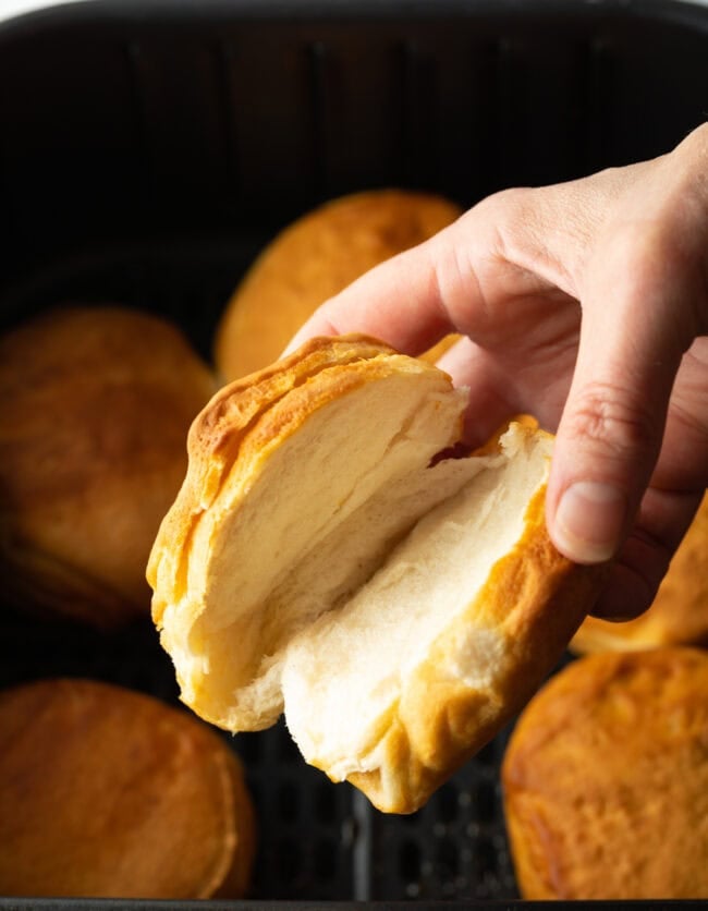 Hand holding air fryer canned biscuit to camera, half open to show inside.