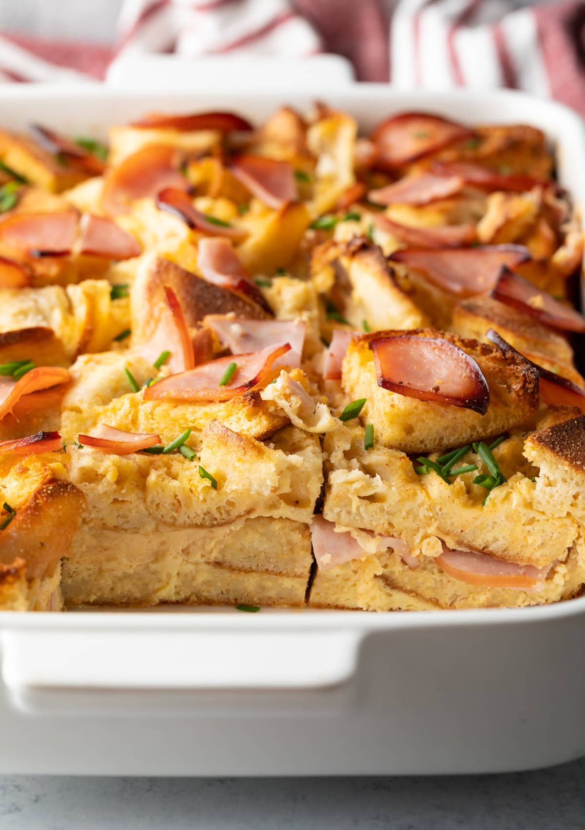 Eggs benedict in a casserole dish. A serving has been removed to show the inside layers of English muffins and Canadian bacon.