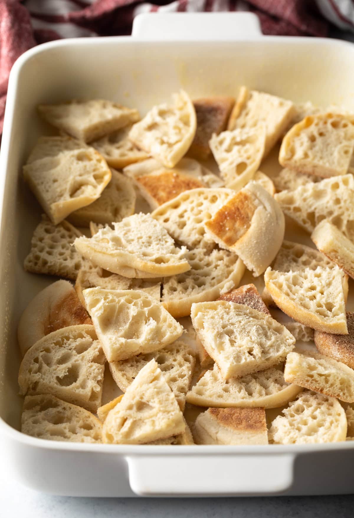 English muffins that have been quartered and layered in a white baking pan.