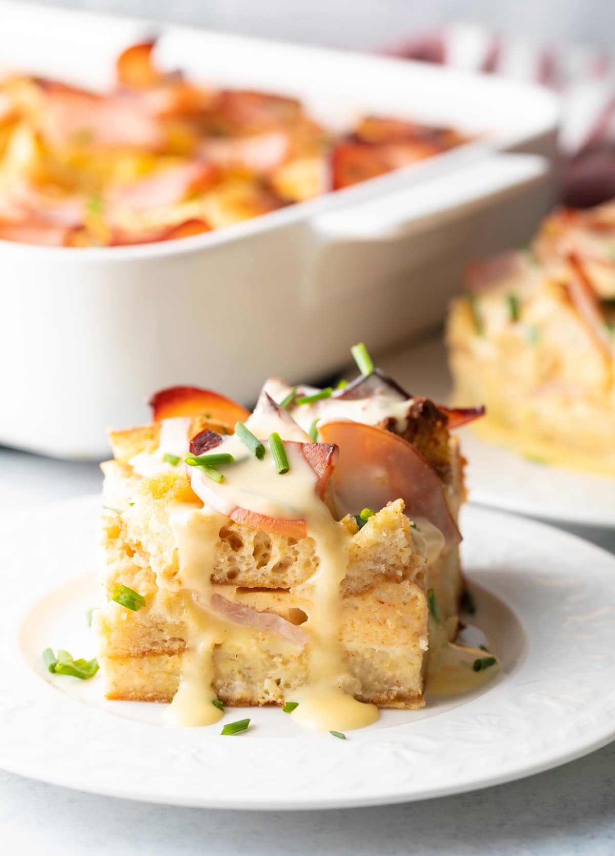 Close view of a slice of breakfast casserole with eggs, Canadian bacon, English muffins and hollandaise sauce.