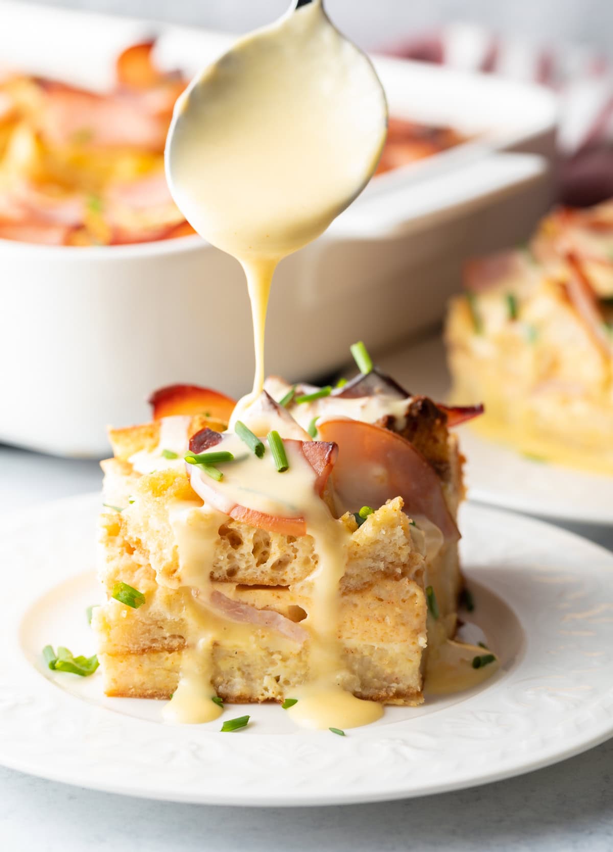 Slice of eggs benedict casserole with hollandaise being drizzled over it with a spoon.