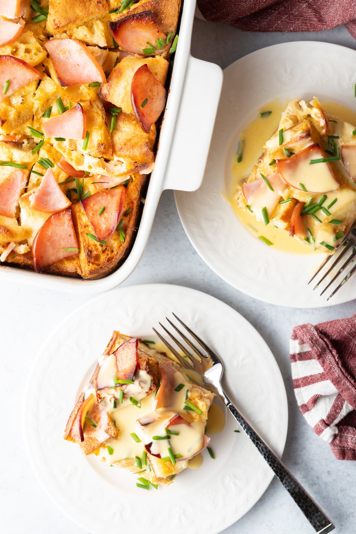 Overhead shot of slices of eggs benedict breakfast casserole on white plates.