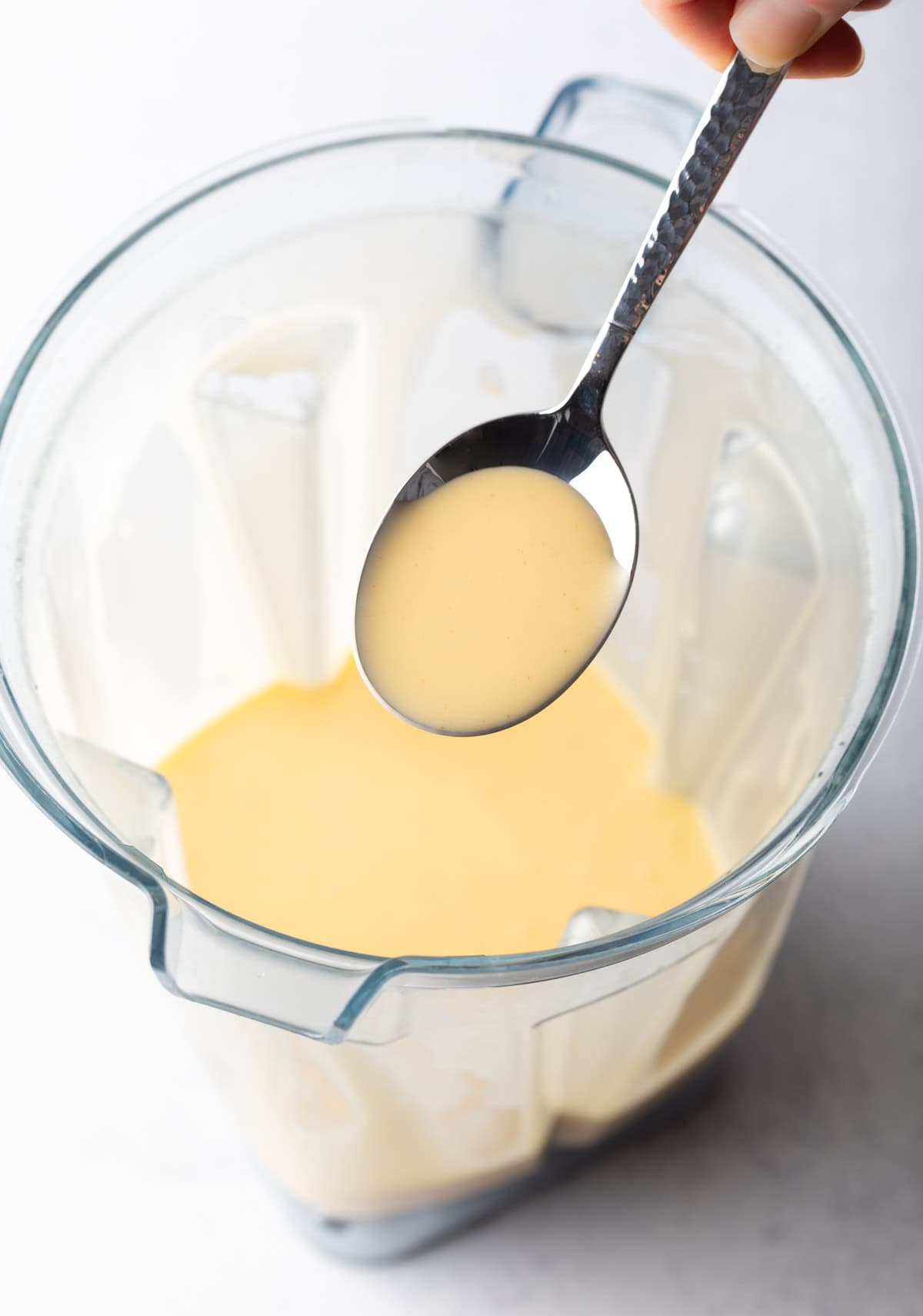 A spoon holding Hollandaise sauce over a blender.
