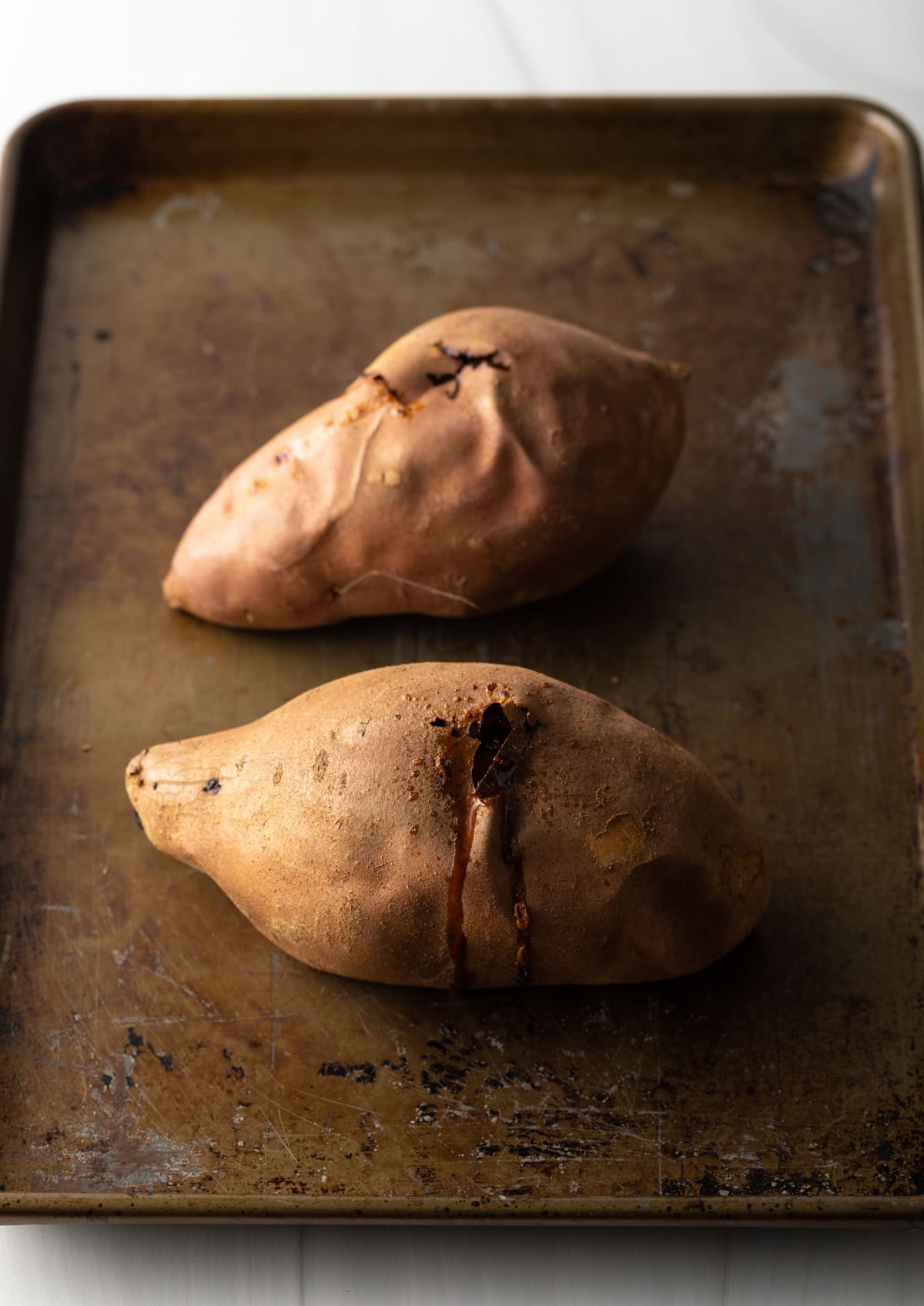 Two baked sweet potatoes on a baking sheet.
