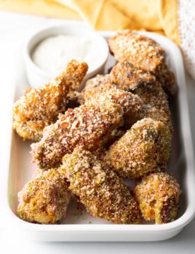Crispy baked chicken wings on a white serving platter with ramekin of caesar dressing.